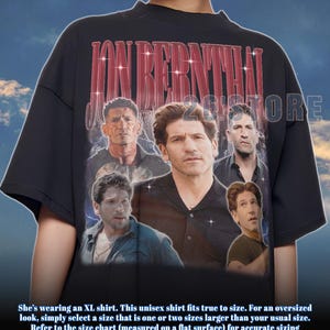 May include: Black unisex t-shirt featuring a collage of images of Jon Bernthal with the text "JON BERNTHAL" in red. The shirt has short sleeves and a crew neck. The text at the bottom of the image says "She's wearing an XL shirt. This unisex shirt fits true to size."