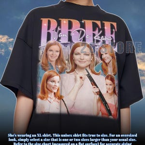Może przedstawiać: Czarny t-shirt unisex z grafiką kobiety z rudymi włosami i napisem "BREE Van De Kamp". Grafika zawiera wiele zdjęć kobiety. Koszulka jest w rozmiarze oversize.