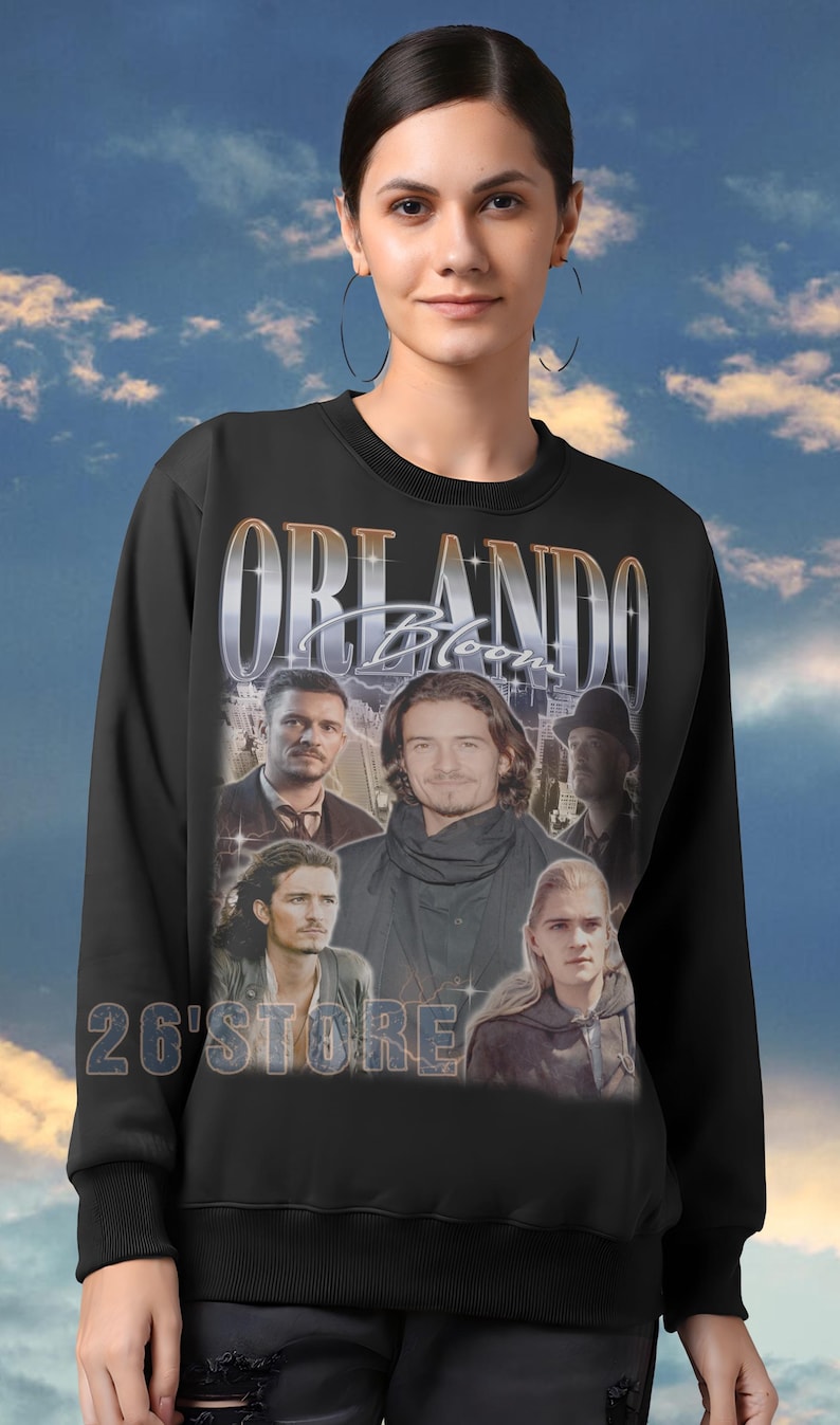 May include: Black crewneck sweatshirt featuring a collage of images of Orlando Bloom, with the name "ORLANDO Bloom" in a silver font. The text "26'STORE" is printed below the collage.