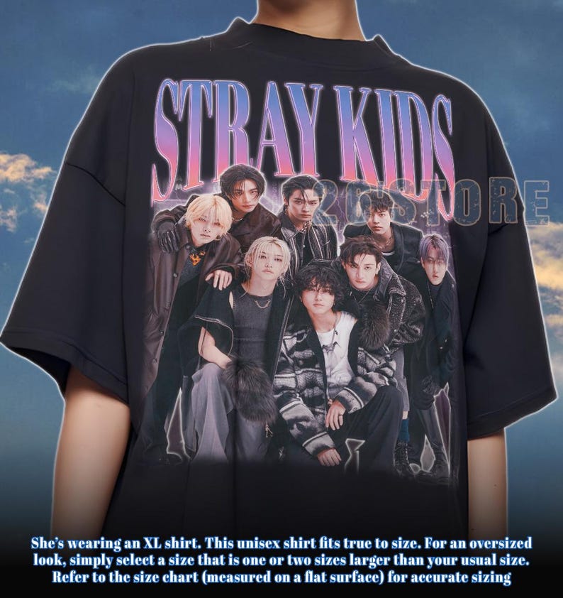 May include: Black oversized t-shirt featuring the text "STRAY KIDS" in a gradient font. The shirt displays a group photo of several people. The shirt is a unisex style.