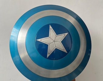 May include: A round, blue and silver shield with a white star in the center. The shield has concentric circles of blue and silver. The shield is a prop or costume piece.