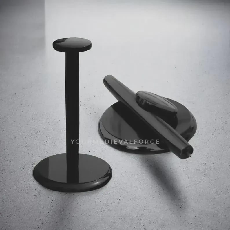 May include: Two black metal display stands. One stand is upright with a circular base and top. The other stand is a flat circular base with a curved arm and a small oval-shaped top. The stands are on a light grey surface.