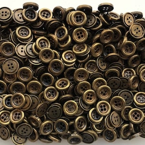 May include: A large pile of gold-toned metal buttons with four holes each. The buttons are arranged in a random pattern.