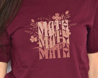 Puede incluir: Una camiseta de color burdeos con un diseño floral y el texto "Math Math Math" en un degradado de rosa y marrón.