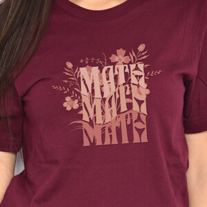 Puede incluir: Una camiseta de color burdeos con un diseño floral y el texto "Math Math Math" en un degradado de rosa y marrón.