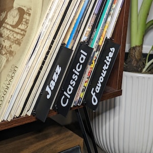 May include: A wooden shelf with vinyl records organised by genre. The labels are "Jazz", "Classical", and "Favourites".