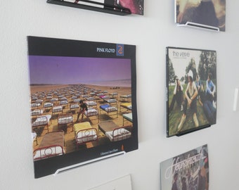 May include: A wall display of vinyl records with black and white album covers. The records are displayed on black and white wall mounts. The album covers feature bands such as Pink Floyd, The Verve, and Fleetwood Mac.