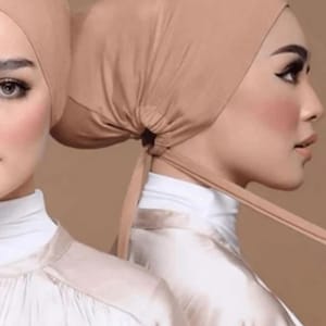 May include: Two women wearing brown headscarves with a tie at the back. The headscarves are made of a soft, stretchy fabric. The women are wearing white shirts.