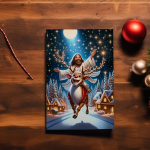 May include: A Christmas card illustration depicts a figure with long hair riding a reindeer through a snowy village under a starry sky. The card is surrounded by Christmas ornaments and greenery on a wooden surface.