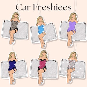 May include: Car Freshie air fresheners featuring illustrations of women in lingerie holding a sparkly rectangle. The air fresheners come in various colors, including blue, purple, pink, and a leopard print design. The text "Car Freshiees" is at the top.
