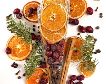 May include: A clear plastic cone filled with dried orange slices, red berries, and cloves, tied with twine. The cone is surrounded by loose dried orange slices, sprigs of green pine needles, cinnamon sticks, red berries, and whole cloves.