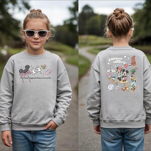 以下が含まれることがあります： ミッキーマウスと他のディズニーキャラクターが描かれたグレーのスウェットシャツ。「The Most Magical Place On Earth」の文字とミッキーマウスの耳、白いウサギなどのグラフィックが前面にプリントされています。背面には、ディズニーキャラクターの大きなグラフィックがあります。