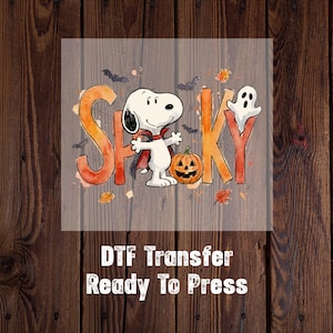 May include: A DTF transfer featuring a cartoon dog dressed as a vampire standing next to a jack-o'-lantern. The word SPOOKY is written in large orange letters with a ghost replacing the letter O. Bats and autumn leaves surround the central design.