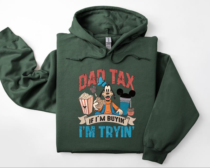 Pode incluir: Uma camisola com capuz verde-floresta escuro com um gr&aacute;fico da personagem Pateta a segurar um snack. O texto DAD TAX IF I'M BUYIN' I'M TRYIN' est&aacute; escrito em letras vermelhas e azuis desgastadas, acompanhado por ilustra&ccedil;&otilde;es de pipocas e uma bebida.