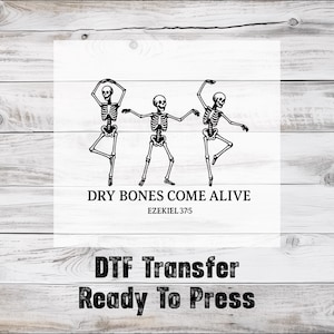 May include: Black and white graphic of three dancing skeletons on a white background. The text "DRY BONES COME ALIVE" and "EZEKIEL 37:5" are below the skeletons. The words "DTF Transfer Ready To Press" are at the bottom.