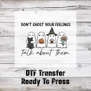 May include: A DTF transfer ready to press, featuring a design with four cartoon ghosts. One ghost holds a black cat, another a pumpkin, a third a coffee cup, and the last a bouquet. The text reads "Don't ghost your feelings, talk about them."