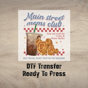 May include: DTF transfer featuring a retro design with the text "Main Street Moms Club." The image includes a coffee drink, Mickey Mouse waffles, and the phrase "Stop and smell the Coffee & Mickey Waffles."
