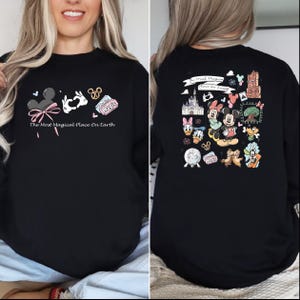 以下が含まれることがあります： ミッキーマウスの耳、ハートを作る手、そして「Magic」と書かれたチケットが描かれた黒いスウェットシャツ。「The Most Magical Place On Earth」の文字が前面にプリントされています。背面には、さまざまなディズニーキャラクターのイラストがあります。