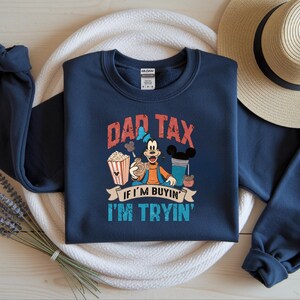 Pode incluir: Uma camisola azul-marinho de manga comprida com um gr&aacute;fico da personagem de desenhos animados Pateta a segurar uma bolacha, ao lado de um balde de pipocas e uma bebida. O texto diz DAD TAX IF I'M BUYIN' I'M TRYIN' em letras vermelhas, brancas e azuis.