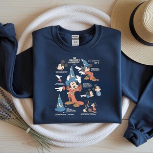 Puede incluir: Una sudadera azul marino de manga larga con un estampado gr&aacute;fico de Mickey Mouse como el aprendiz de brujo. El dise&ntilde;o incluye varios bocetos del personaje y el texto The Sorcerer's Apprentice, Walt Disney Prod y RX-1.