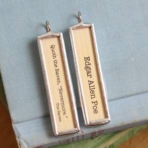 May include: Two silver framed bookmarks with a quote from Edgar Allan Poe's "The Raven" and his name on the other. The bookmarks are on a blue book.