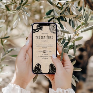 K&ouml;nnte beinhalten: Ein Smartphone zeigt eine Einladung im Vintage-Stil f&uuml;r die Veranstaltung "The Traitors Castle" am 31. Oktober um 22:00 Uhr. Das Design zeigt eine Maske, einen Kompass und Kapuzenfiguren vor einem Pergamenthintergrund. Das Telefon wird vor einem verschwommenen nat&uuml;rlichen Hintergrund gehalten.
