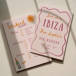 Può includere: Due biglietti rosa per l'itinerario dell'evento. Una carta presenta il testo "The Weekend Itinerary" con un'illustrazione del sole. L'altra carta dice "Join us in Ibiza For Sophie's Hen Weekend July 28th-31st 2026".