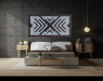 May include: A white bed with a brown headboard and a white geometric wooden wall hanging above it. The bed is in a room with a concrete wall and a wooden nightstand on each side. There is a small plant on each nightstand and a hanging light fixture above the bed.