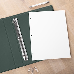 May include: A dark green three-ring binder with a metallic silver mechanism, featuring a single blank white sheet of paper with three punched holes. A white ballpoint pen lies horizontally above the binder, and three silver paper clips are below.