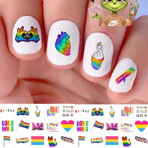 以下が含まれることがあります： レインボーハート、旗、解剖学的な心臓、PRIDE、LOVE WINS、LOVE IS LOVEなどのテキストを含む、様々なプライドをテーマにしたデザインのネイルデカールシート。白いマニキュアを塗った爪に貼った例が示されています。