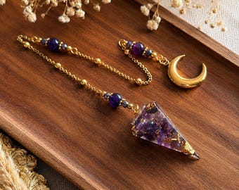 May include: A pendulum featuring a conical resin point filled with purple amethyst chips and gold flakes, attached to a gold-tone chain. The chain includes purple beads and a gold-tone crescent moon charm at the end, creating a decorative accessory.