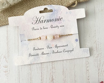 Peut inclure: Un bracelet en chaîne dorée avec trois perles roses et blanches. La carte indique "Harmonie", "Pierre de lune - Quartz rose", "Tendresse - Paix - Apaisement", et "Féminité - Amour - Bonheur Conjugal".