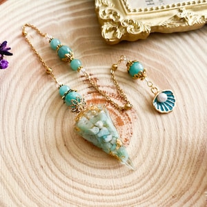 May include: A gold chain with a green crystal pendulum. The pendulum is filled with smaller green crystals and gold flakes. The chain has a green crystal bead and a gold shell charm.