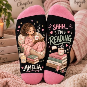 Pode incluir: Meias pretas com calcanhares e pontas cor-de-rosa, com a imagem de uma pessoa a ler numa poltrona com o nome Amelia, e o texto SHHH... I'M READING sobre uma pilha de livros com os títulos Chapters & Charm, Cozy Tales, Hearts & Pages, Bookish Escapes.