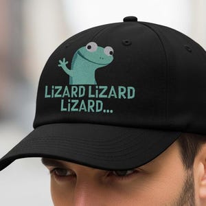 May include: Black baseball cap with a lizard graphic and the text "Lizard Lizard Lizard...". The lizard is light blue with white eyes. The cap has a curved brim and a button on top.