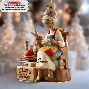 May include: A decorative ornament featuring a woman quilting, seated in a wooden chair. She wears a white dress with a colorful patchwork skirt and red apron. The ornament includes the text "Quilting is my Therapy" and the name "Emma".