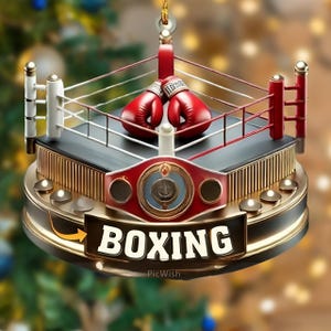 May include: A decorative boxing-themed ornament featuring a miniature boxing ring with red gloves. The ornament has a gold base with the word "BOXING" in white lettering. A red championship belt is also featured.