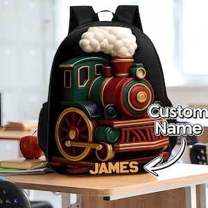 May include: Black backpack featuring a 3D train design in red, green, and gold. The train has a white smoke effect and the name "JAMES" is displayed. The words "Custom Name" are also visible.