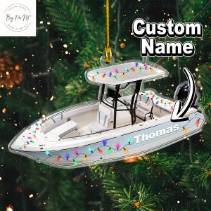 May include: A white and light blue boat ornament with the name "Thomas" and a string of colorful lights. The ornament has a white top and is hanging from a gold string. The words "Custom Name" are at the top.
