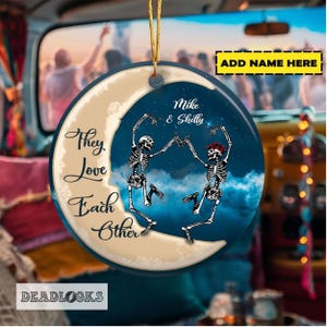May include: A round, cream-colored ornament with a blue crescent moon and two skeletons dancing. The text "They Love Each Other" is written on the ornament. The text "Mike & Shelly" is written on the ornament.