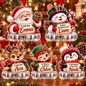 May include: Five clear acrylic Christmas ornaments featuring Santa, a snowman, a reindeer, an elf, and a penguin. Each ornament holds a rolled-up dollar bill and a sign with names including Emma, Liam, Ava, Chloe, and Noah, plus holiday text.