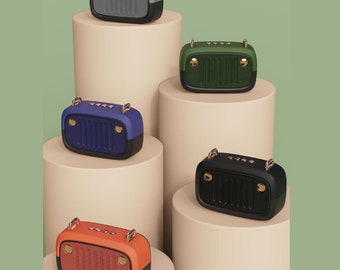 May include: Five retro-style portable speakers in different colors, displayed on beige cylindrical stands. The speakers have a vintage car grille design and are available in blue, green, black, orange, and gray.