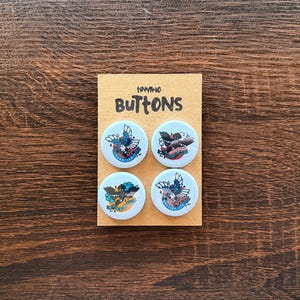 May include: Four round buttons with bird designs on a light blue background are displayed on a brown card. The card reads "tiny-10 BUTTONS" in black letters. The buttons have colorful illustrations of birds.