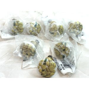 May include: A collection of seven round cabinet knobs. Each knob features a white base with a yellow floral design and a metal stem. The knobs are individually packaged in clear plastic.