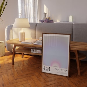 May include: A framed poster with a gradient background of pink, purple, and blue. The poster has the number 444 and the word "PROTECTION" printed on it. The poster is leaning against a wooden coffee table with books and a lamp on it.