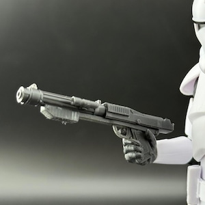 May include: A white action figure of a soldier in a helmet and armor, holding a gray blaster gun. The figure is set against a gray background. The soldier's helmet has a black visor and blue accents.