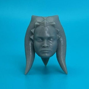 Könnte beinhalten: Eine graue, 3D-gedruckte Kopfskulptur einer fiktiven Figur mit einer markanten Frisur. Die Figur hat einen ernsten Ausdruck und trägt ein Kopfstück mit komplizierten Details.