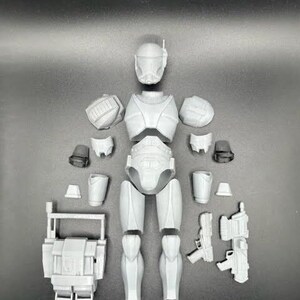 May include: A white plastic model kit of a Star Wars clone trooper. The kit includes the head, torso, arms, legs, and weapons. The model is unassembled and ready to be built.