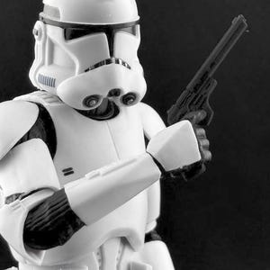 以下が含まれることがあります： SFシリーズのクローン・トルーパーの白黒アクションフィギュア。フィギュアは黒いブラスターピストルを持っています。トルーパーは白いヘルメットと黒いアクセントのアーマーを着用しています。背景は黒です。