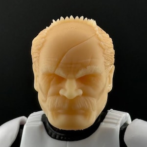 May include: A detailed action figure head with a realistic, aged appearance. The figure has a light skin tone, a prominent mustache, and a scar across the forehead. The figure is wearing a white and black uniform.
